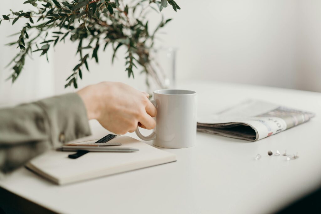 Embrace the small rituals. A close up of hands holding coffee mugnear a window, steam rising and a natural light falling softly.